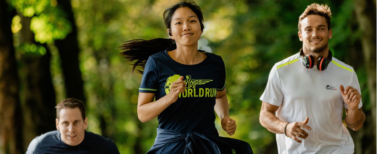 Trīs skrējiena &ldquo;Wings for Life World Run&rdquo; dalībnieki priecīgi skrien; ausīs tiem ir Philips sporta austiņas.